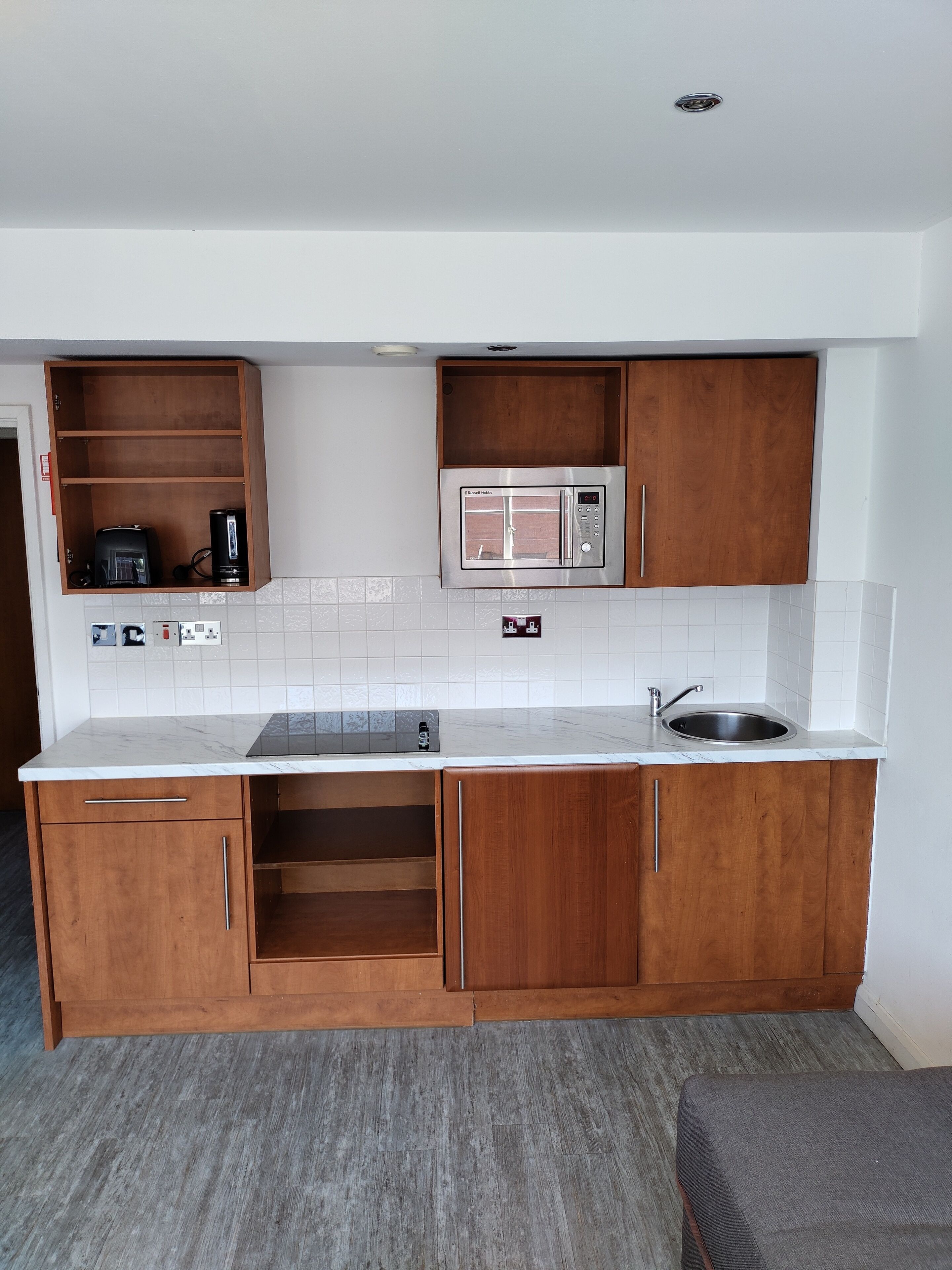 A compact kitchen with wooden cabinets, a built-in microwave, and a stainless steel sink.