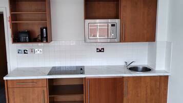 A compact kitchen with wooden cabinets, a built-in microwave, and a stainless steel sink.
