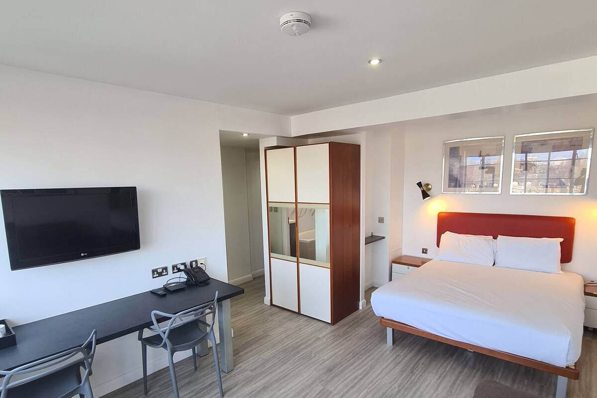 A hotel room with a bed, a desk with a chair, a TV, and a wardrobe.