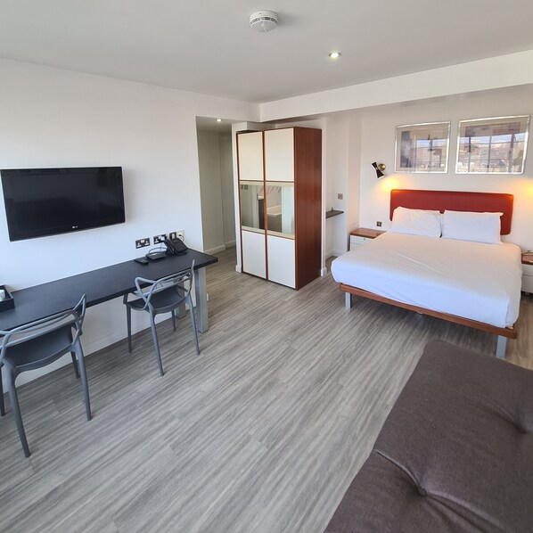 A hotel room with a bed, a desk with a chair, a TV, and a wardrobe.