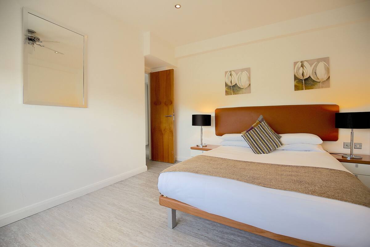 A hotel room with a bed, bedside tables, a wooden door, and artwork on the walls.