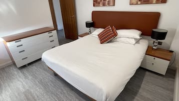 Un dormitorio moderno con una cama grande, cabecera de madera, dos mesitas de noche con lámparas, un aparador y arte abstracto en la pared.