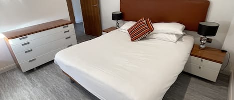 Un dormitorio moderno con una cama grande, cabecera de madera, dos mesitas de noche con lámparas, un aparador y arte abstracto en la pared.