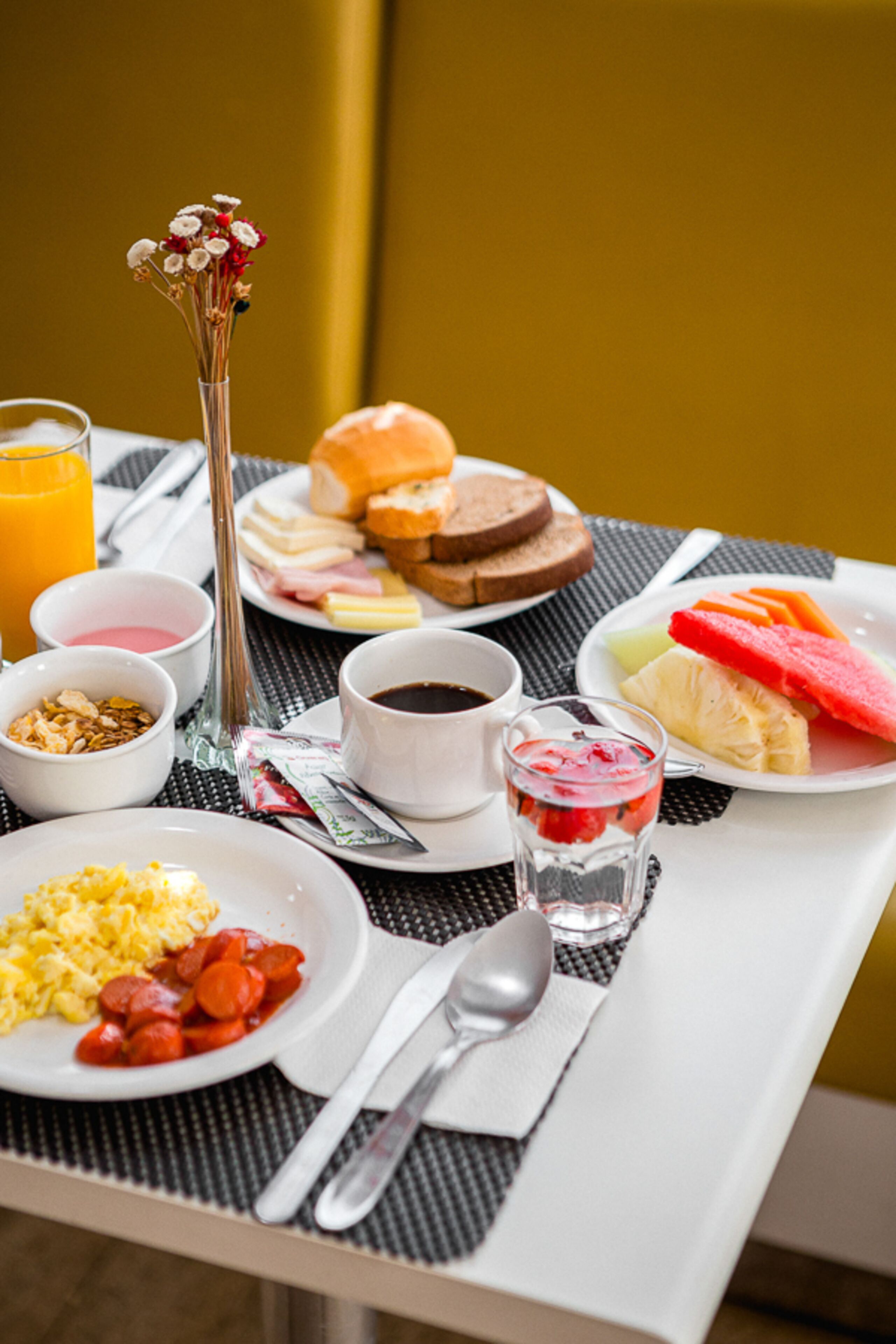 Una mesa de desayuno con diversos alimentos, entre ellos tostadas, huevos y fruta, además de tazas de café y jugo.