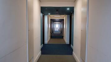 Un pasillo largo y estrecho con piso alfombrado y puertas a ambos lados que dan a habitaciones.