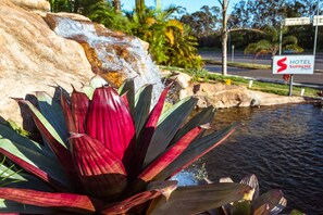A hotel sign with a red 'S' logo, a pond, and red and green foliage. - VOA Business Supreme Choice Confins (Lagoa Santa)