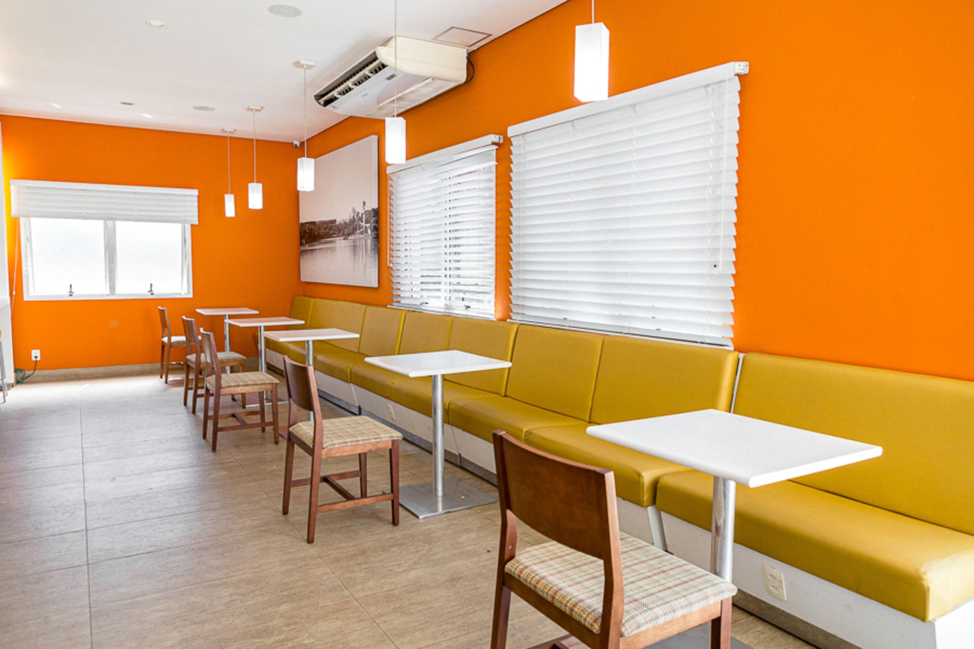 Un restaurante con paredes naranjas, mesas blancas y sillas de madera.