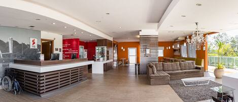 A modern hotel lobby with a reception desk, seating area, and a view of the outdoors.