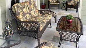 Un'area patio coperta con mobili in vimini, una pianta in vaso e un quadro appeso al muro.