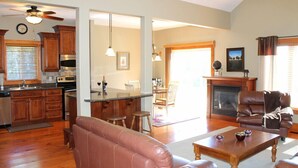 Un'ampia zona giorno con divano in pelle, tavolino in legno e camino. È presente una cucina con mobili in legno e una sala da pranzo con tavolo e sedie.