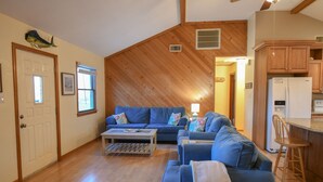 Un salon chaleureux avec un canapé bleu, un plafond en bois et un coin cuisine doté de meubles en bois et d’un réfrigérateur.