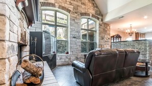 A stone fireplace with a black leather sofa and a log fire. - Lake Travis Acreage with Hilltop Views  (Austin)