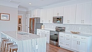 Una cocina moderna con armarios blancos, electrodomésticos de acero inoxidable, una isla de mármol con taburetes y un salpicadero con diseño.