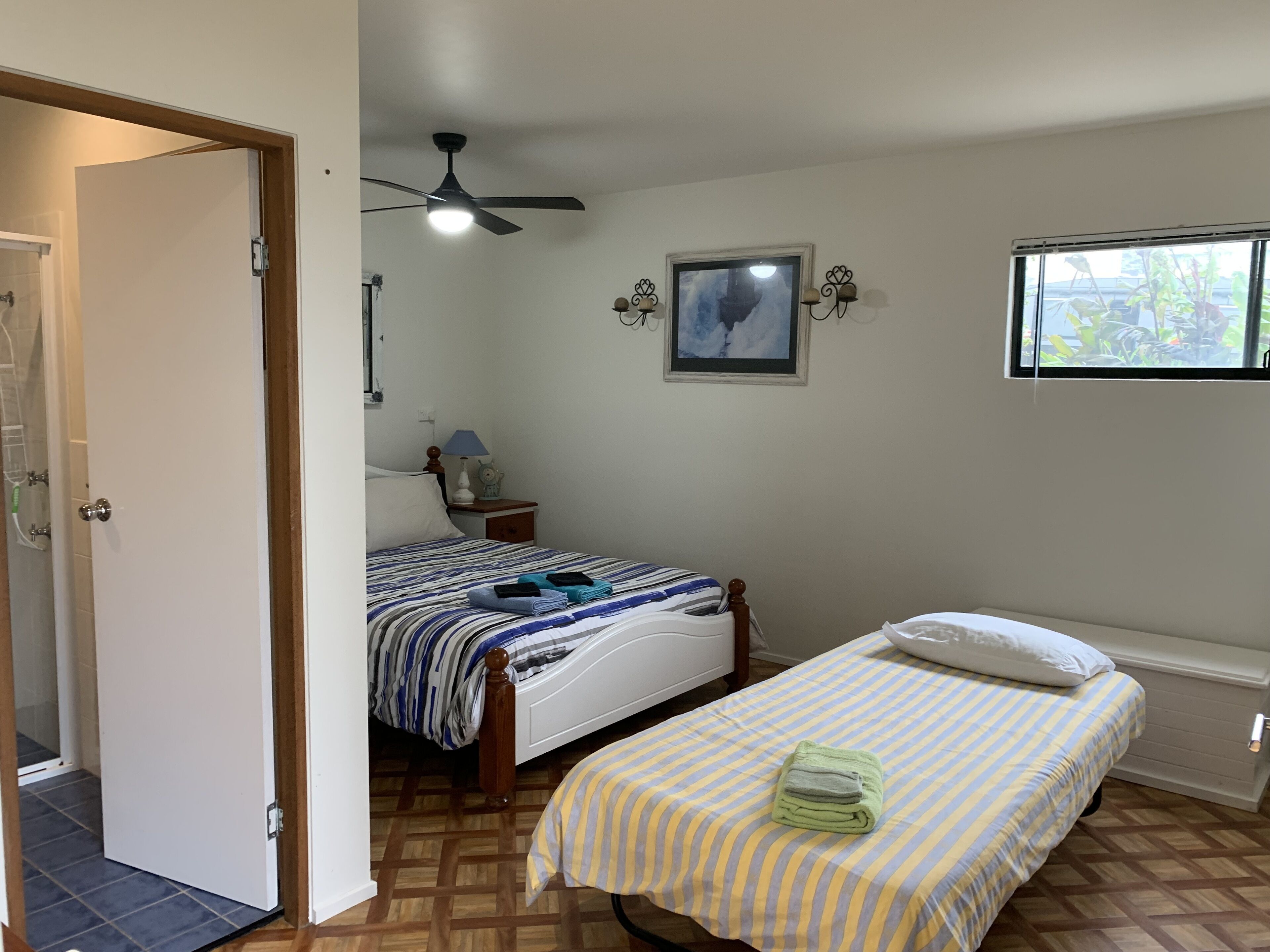 A bedroom with a bed, a bedside table, a lamp, a ceiling fan, a window, and a door.