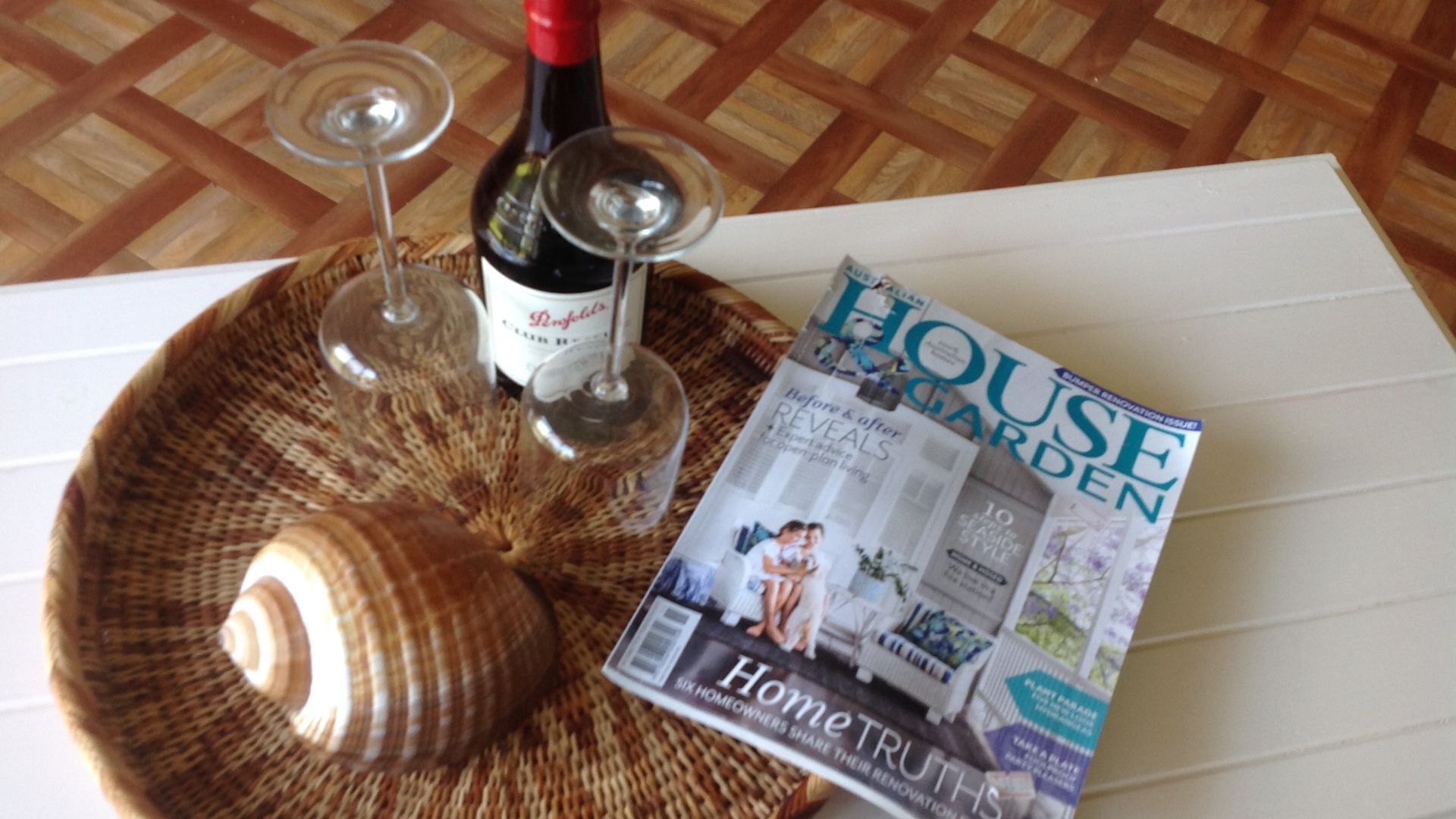 A magazine titled "HOUSE GARDEN" on a table with a woven placemat, a wine bottle, and two wine glasses.
