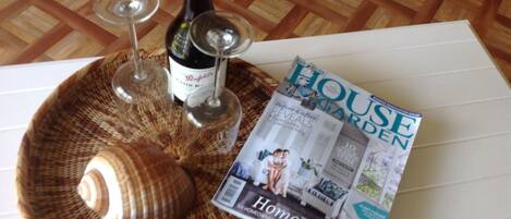A magazine titled "HOUSE GARDEN" on a table with a woven placemat, a wine bottle, and two wine glasses.