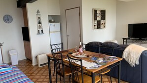 Un coin repas avec une table en bois, des chaises et un téléviseur en arrière-plan.