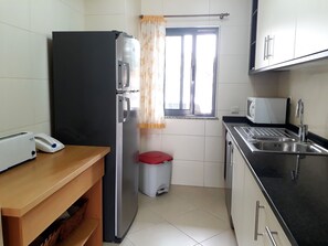 A compact kitchen with a refrigerator, microwave, toaster, sink, and a small trash bin.