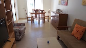 A living room with a sofa, a coffee table, a TV, a dining table with chairs, and a cabinet. - Tahiti- Spacious, Private Parking, Terrace with Sunbeds, 300 meters Beach (Quarteira)
