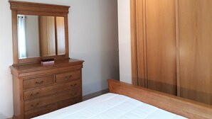 A bedroom with a wooden dresser, a mirror, a bed, and a wardrobe. - Tahiti- Spacious, Private Parking, Terrace with Sunbeds, 300 meters Beach (Quarteira)