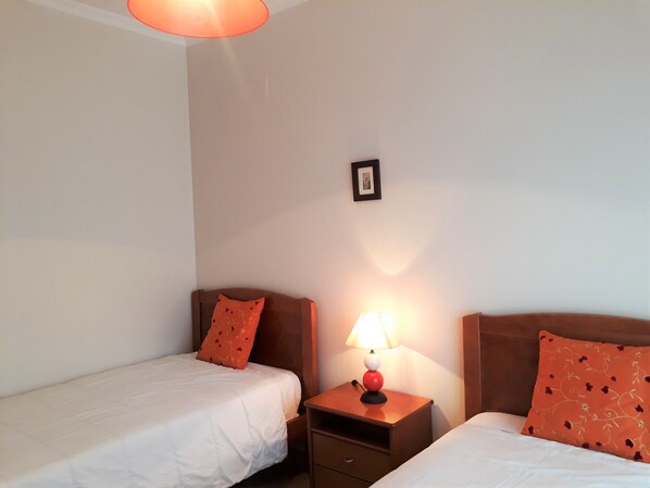 A hotel room with two single beds, a nightstand with a lamp, and a small picture on the wall.