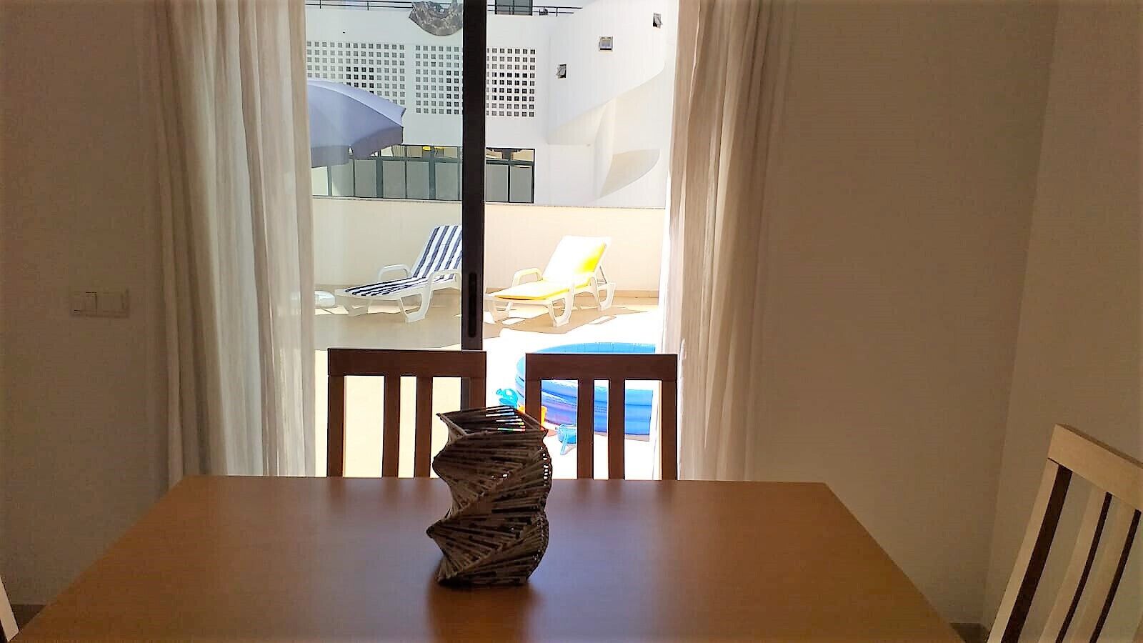 Una mesa de comedor con un original centro de mesa, una ventana con cortinas y vistas a un área de estar al aire libre.