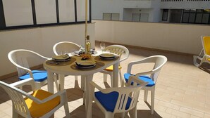 A round table with white chairs, some with blue cushions, set on a tiled patio. - Tahiti- Spacious, Private Parking, Terrace with Sunbeds, 300 meters Beach (Quarteira)