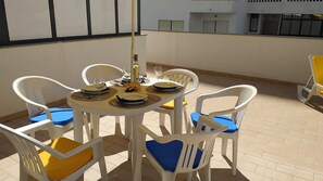 A round table with white chairs, some with blue cushions, set on a tiled patio.