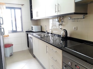 A kitchen with white cabinets, a black countertop, a microwave, a kettle, and a dishwasher. - Tahiti- Spacious, Private Parking, Terrace with Sunbeds, 300 meters Beach (Quarteira)