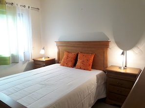 A neatly made bed with a wooden headboard, two bedside lamps, and a nightstand with a lamp.
