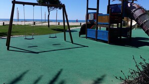 A playground with swings and a slide, set against a beach backdrop. - Tahiti- Spacious, Private Parking, Terrace with Sunbeds, 300 meters Beach (Quarteira)