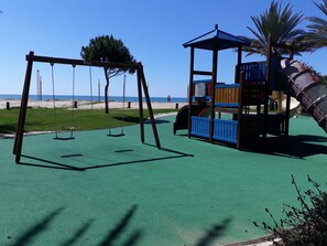 A playground with swings and a slide, set against a beach backdrop. - Tahiti- Spacious, Private Parking, Terrace with Sunbeds, 300 meters Beach (Quarteira)