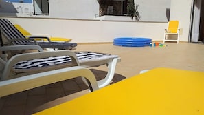 A patio with sun loungers and a yellow table, a blue inflatable pool, and a yellow chair.