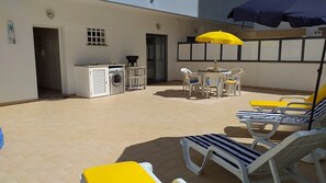An outdoor patio with a washing machine, a barbecue, and a table with chairs. - Tahiti- Spacious, Private Parking, Terrace with Sunbeds, 300 meters Beach (Quarteira)