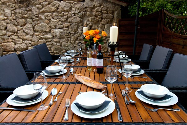 A wooden dining table set for six with white plates, silverware, and a loaf of bread.