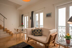 Un soggiorno moderno con un divano, un tavolo da pranzo con sedie, una scala e un balcone con ringhiera.