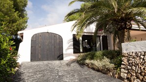 Un chemin de pierres mène à un bâtiment doté d’une grande porte en bois et bordé d’un palmier.