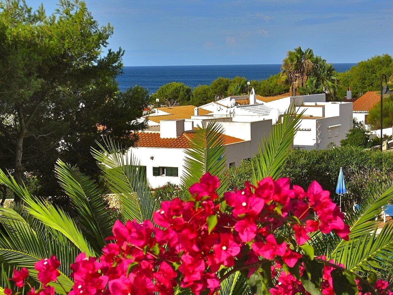 A coastal residential area with white buildings, a clear blue sky, and a view of the sea.