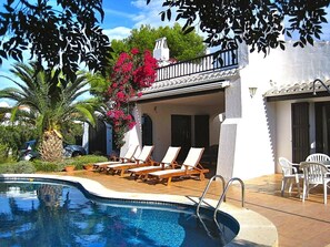 A pool area with lounge chairs, a palm tree, and a building with a balcony. - Top rated Menorca villa. Sleeps 5, Air Con, Private Pool, Walk to sea /village (Binibequer Vell)