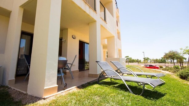 A building with a covered outdoor area, including a table and chairs, and a lawn with sun loungers. - Modern, accessible ground floor apartment just 30 minutes from Murcia airport (Corvera, Murcia)