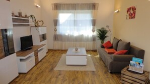 Una sala de estar moderna con un televisor de pantalla plana, una mesa de centro blanca, un sofá gris con cojines rojos y un aparador de madera.