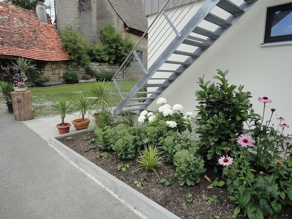 A garden with various plants and flowers, a wooden post, and a metal staircase.