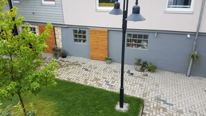 Ett modernt hus med en grå fasad, ett tak täckt med takpannor och en stenlagd trädgård med en gräsmatta.