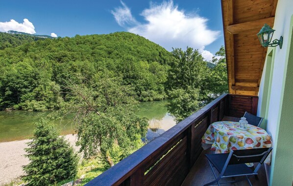 A balcony with a table and chair overlooking a river and forested hills. - Gorgeous home in Brod na Kupi with sauna (Brod na Kupi)