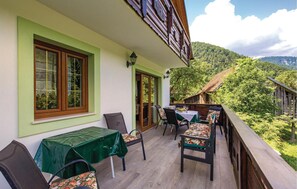 A balcony with a table and chairs, a view of a forested hillside, and a traditional building with wooden beams and a sloped roof. - Gorgeous home in Brod na Kupi with sauna (Brod na Kupi)