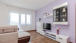 A modern living room with a sofa, TV, and entertainment unit against a purple wall. - Nice apartment in Crikvenica with house sea view (Crikvenica)