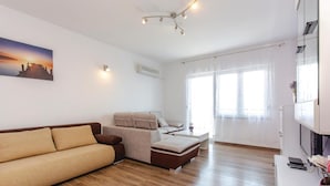 A modern living room with a sofa, a coffee table, and a TV. There is a window with sheer curtains and a painting on the wall. - Nice apartment in Crikvenica with house sea view (Crikvenica)