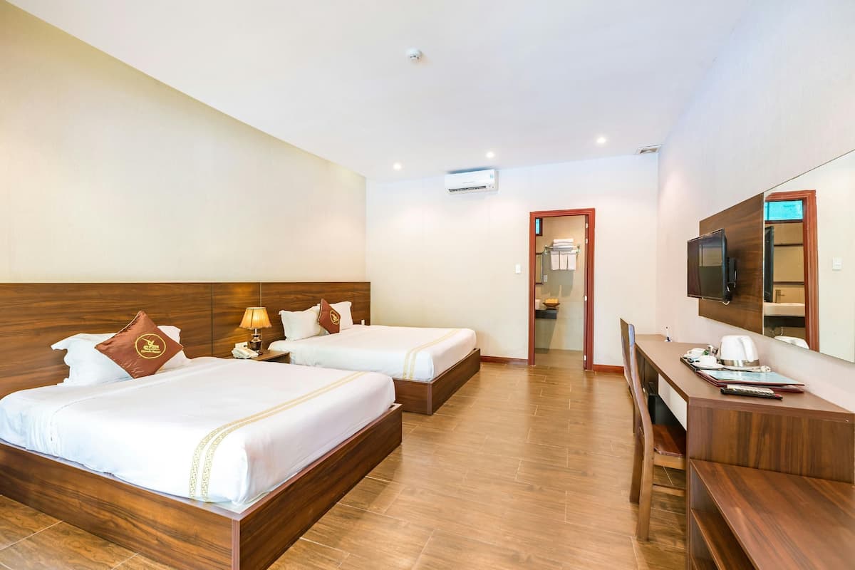 A hotel room with two beds, a desk, a TV, and an air conditioning unit.