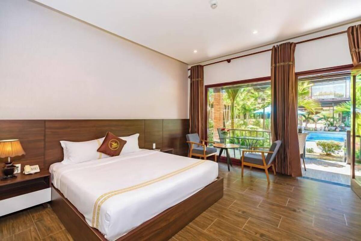A hotel room with a large bed, a nightstand, a desk, a chair, and a view of a pool.