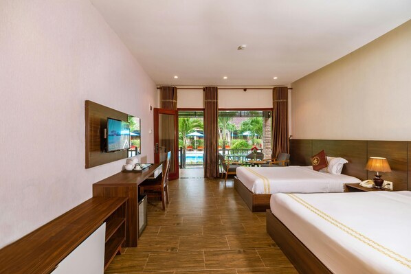 Habitación de hotel con dos camas, un escritorio, televisión y vista al área de la piscina.